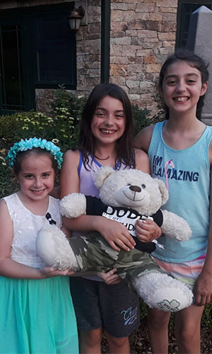 Three girls standing with a stuffed bear