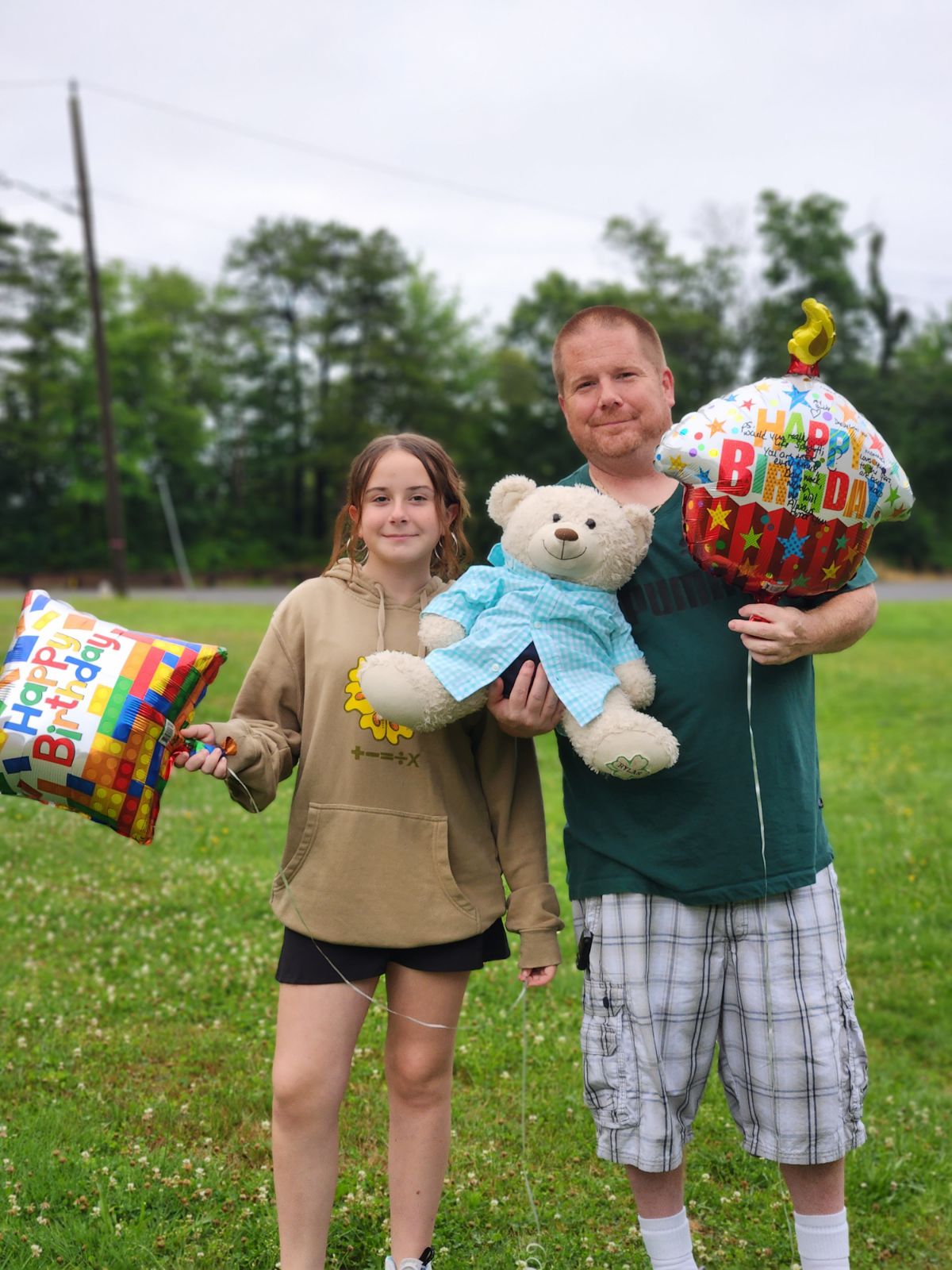 Young girl and man standing with balloons 
            reading Happy Birthday