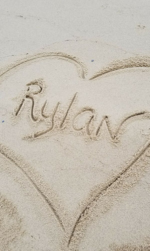 The name Rylan drawn in sand with a heart around it